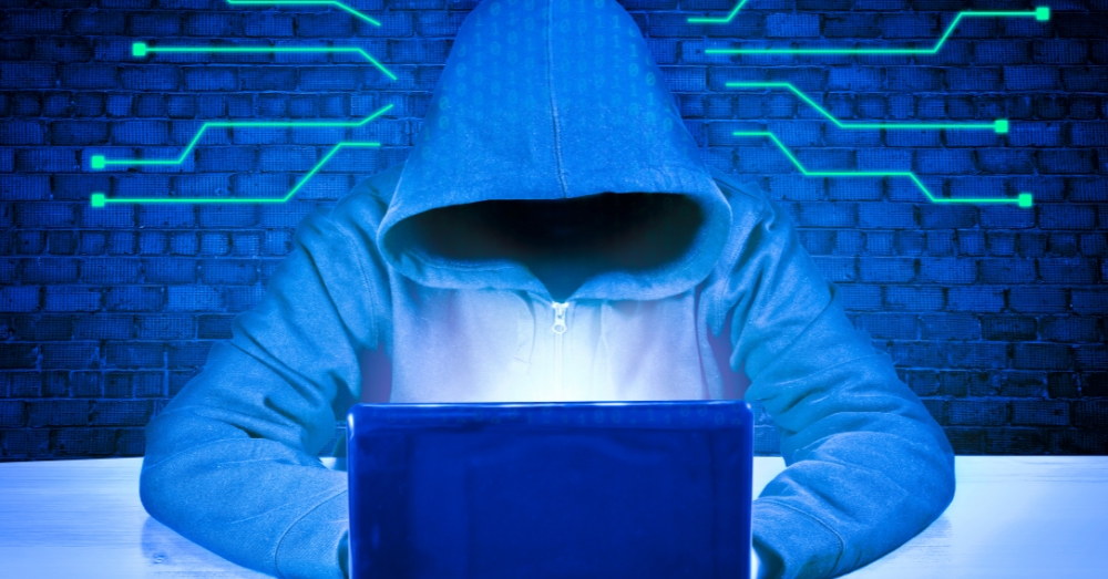 A man in a hoodi with a laptop in a cyber background.